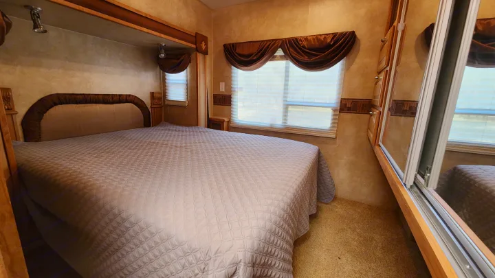 Cozy RV rental bedroom with quilted bed, window, and mirrored sliding closet doors visible.. Forest River Wildcat 2008