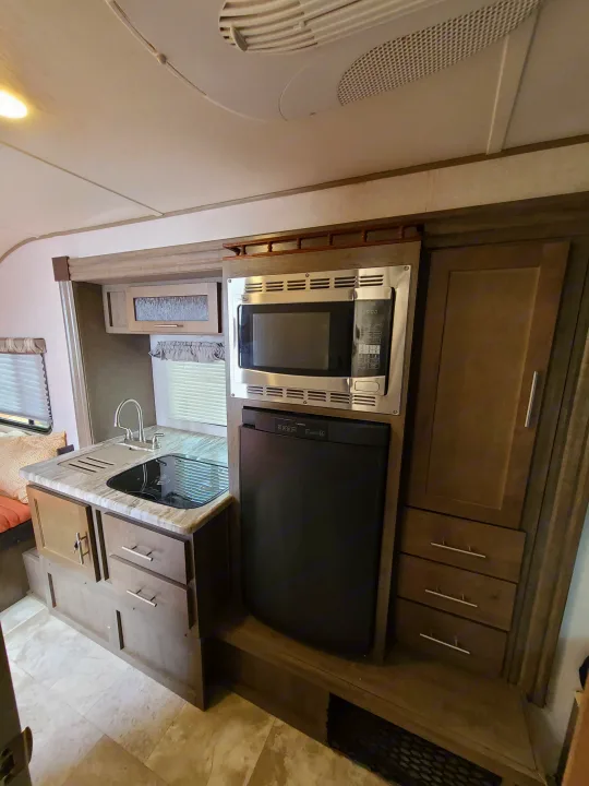 Inside a comfortable RV rental: fully equipped kitchen with sink, microwave, fridge, and cooktop, ready for your mobile home adventures.. Forest River R-Pod 2018