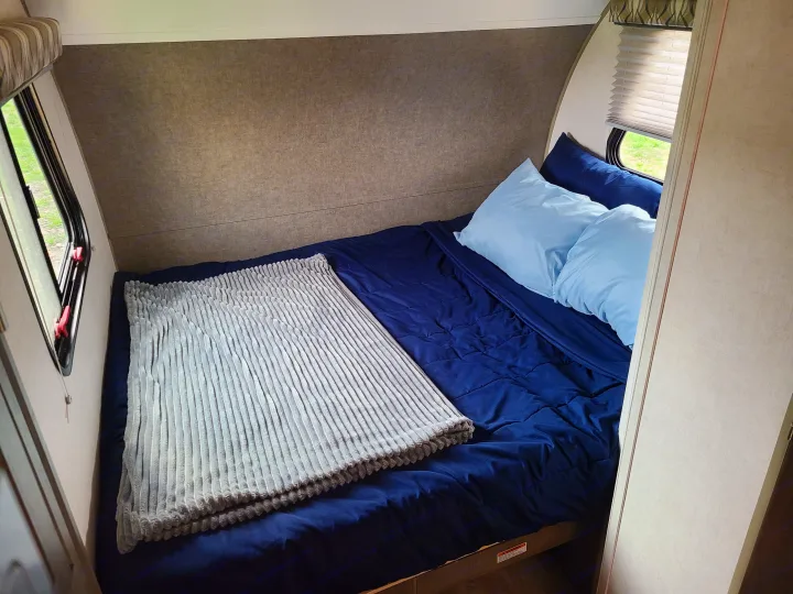 Cozy rv rental bedroom, featuring a neatly made bed with blue linens, pillows, and windows offering outdoor views.. Forest River R-Pod 2018