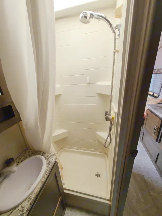 Inside this RV rental: a clean, compact bathroom with a bright shower stall, handheld head, shelves, and a small sink vanity.. Forest River R-Pod 2018