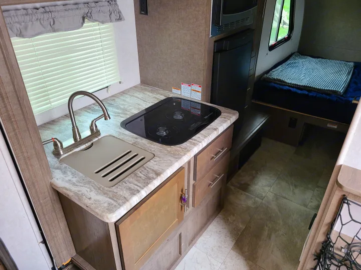 Compact rv rental interior: features kitchen with sink, stove, microwave, fridge, and adjacent sleeping area.. Forest River R-Pod 2018