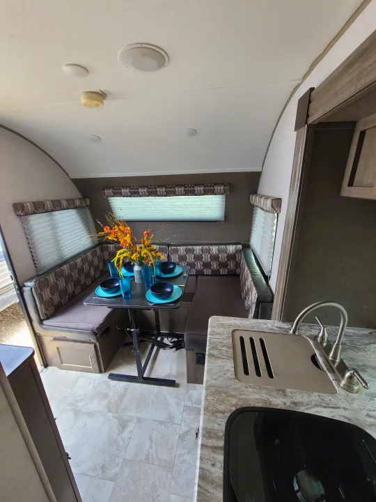 Inside an RV rental: a spacious dinette with U-shaped booth seating, set table, and functional kitchen area.. Forest River R-Pod 2018