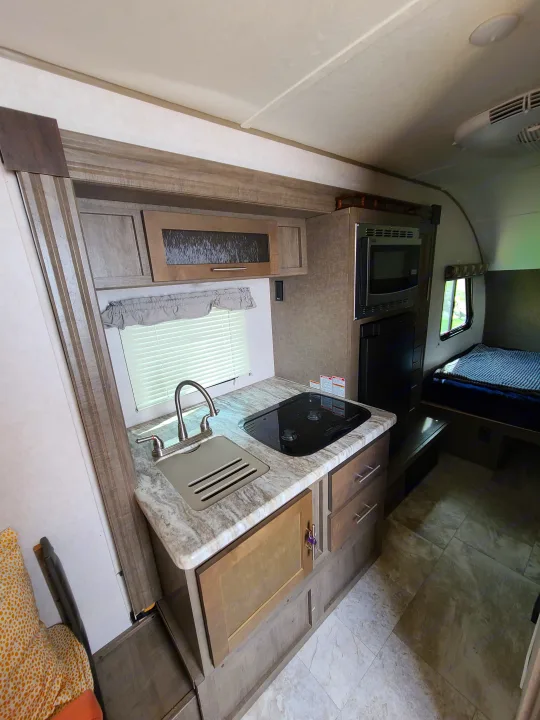 Step into this clean RV rental, offering a compact kitchen with sink, stove, microwave, fridge, and a cozy bed area.. Forest River R-Pod 2018