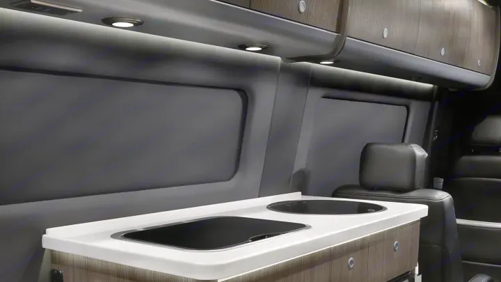 Inside an RV rental: Compact kitchen featuring a sleek cooktop, sink, and overhead storage.. Airstream Interstate 2021