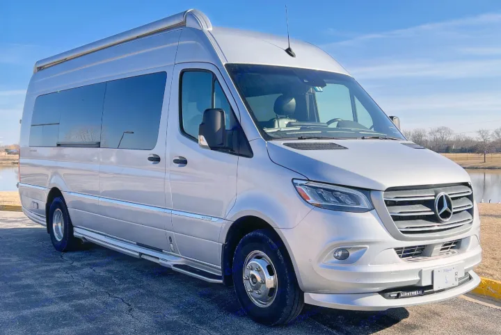 This silver Mercedes-Benz Sprinter Airstream RV rental is ready for adventure, seen by a tranquil lake.. Airstream Interstate 2021