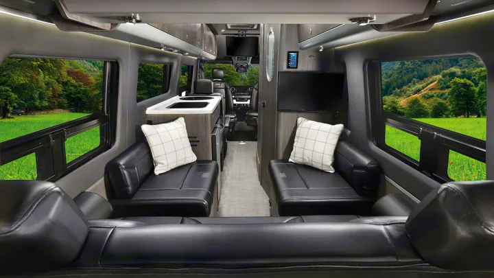 Spacious RV rental interior featuring black leather seating, a compact kitchen, and large windows with serene natural views.. Airstream Interstate 2021
