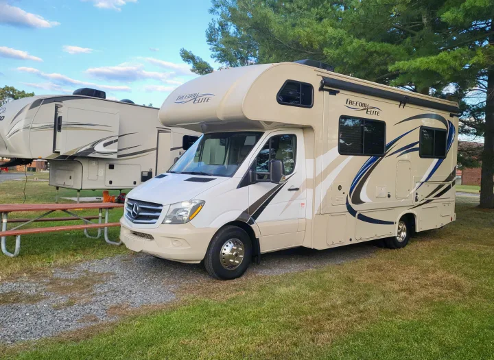 This rv rental, a Class C motorhome, is parked at a campsite next to a fifth-wheel travel trailer, perfect for outdoor adventures.. Thor Freedom Elite 2018