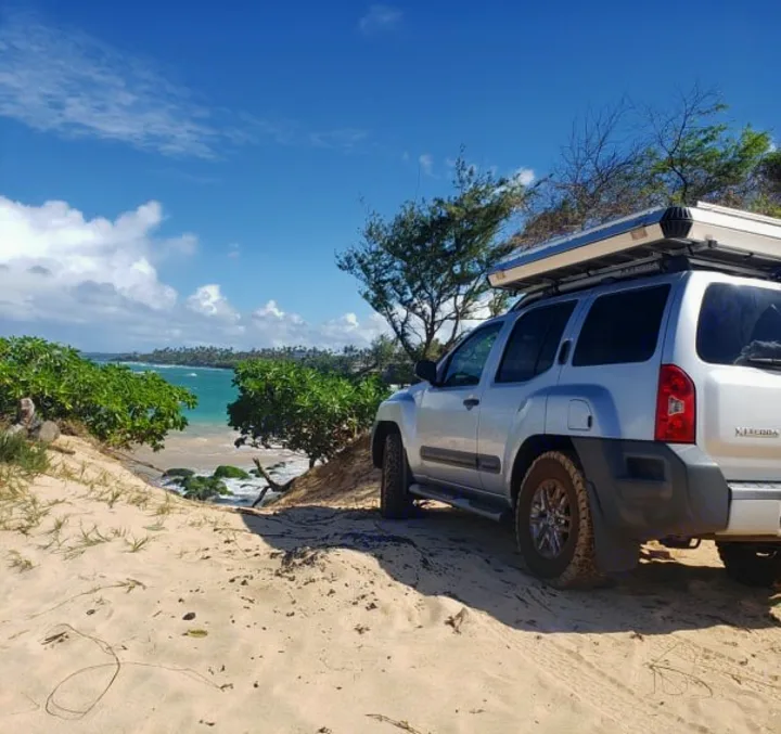 Off-road RV rental adventure! Silver SUV with rooftop tent on a sandy dune overlooking a turquoise beach.. NISSAN XTERRA 2014