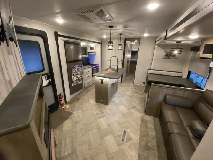 Modern RV rental interior with a spacious kitchen island, stainless steel refrigerator, dining booth, and living area with a couch.. Forest River Palomino Puma 2022