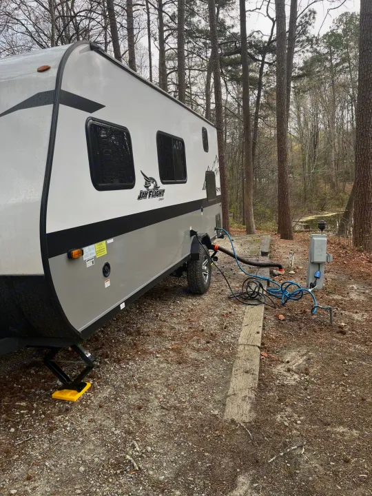 A Jay Flight rv rental camper at a wooded campsite with full hookups visible. Perfect for nature getaways.. Jayco Jay Flight SLX 2022