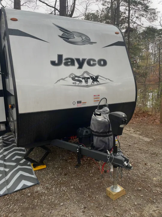 Front of a white Jayco RV rental parked at a lakeside campsite. Visible are the propane tank, hitch, and stabilizing jack.. Jayco Jay Flight SLX 2022