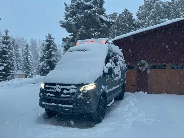Snow-covered Mercedes Sprinter **RV rental** van, headlights illuminating falling snow in a winter scene.. Mercedes-Benz Entegra Launch 2023