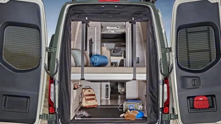 Rear view of an RV rental camper van, doors open, revealing a multi-level interior with bed, organized storage, and gear.. Mercedes-Benz Entegra Launch 2023