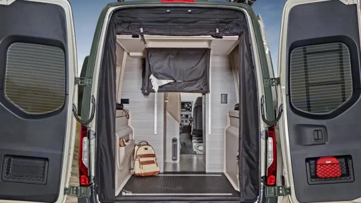 Rear view of an RV rental's interior with open doors, showing ample storage, a backpack, and the cozy living space.. Mercedes-Benz Entegra Launch 2023