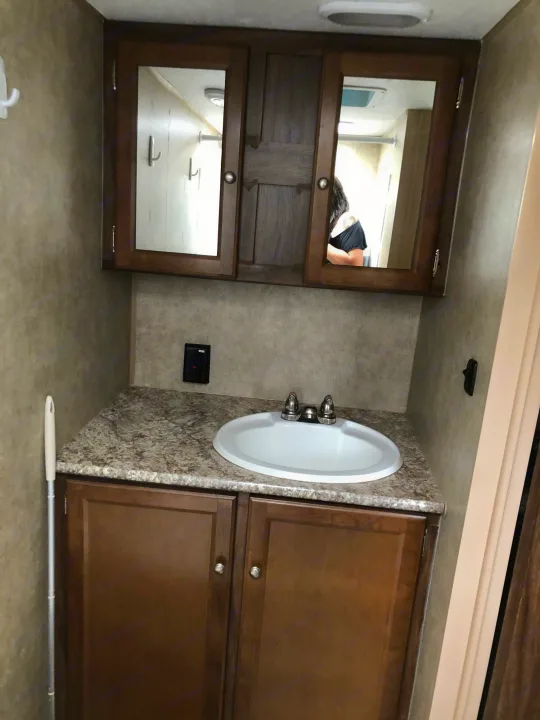 RV rental bathroom: compact vanity with white sink, granite-look counter, wood cabinets, & mirrored medicine cabinet.. Forest River Viking 2018