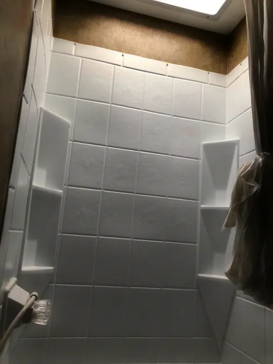 Clean, compact shower in an RV rental, featuring white tile-look walls, built-in shelves, and a clear handle.. Forest River Viking 2018