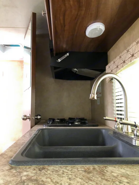 Compact RV rental kitchen with a double sink, stovetop, and overhead lighting, ready for your adventures.. Forest River Viking 2018