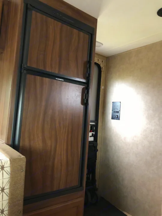 This RV rental interior features a Dometic refrigerator with wood-grain doors, a control panel, and the main entry.. Forest River Viking 2018