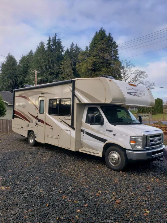 A beige and white Coachmen Leprechaun Class C RV, ideal for an rv rental, parked on a dark gravel driveway.. Coachman Leprechaun 2017