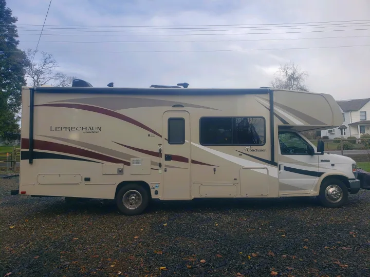 Coachmen Leprechaun Class C RV rental. Beige with stripes, this motorhome is parked on gravel, ready for adventures.. Coachman Leprechaun 2017
