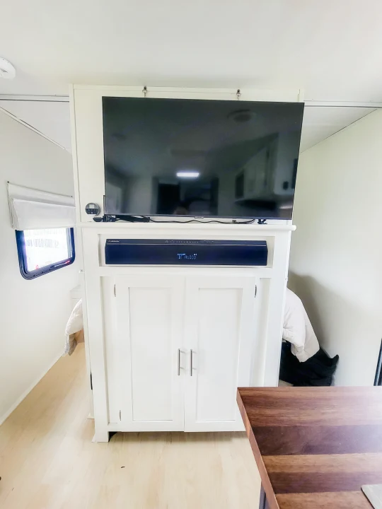 Modern RV rental media center featuring a large TV, Furrion soundbar, white cabinets, and light wood flooring.. Forest River Tracer 2022