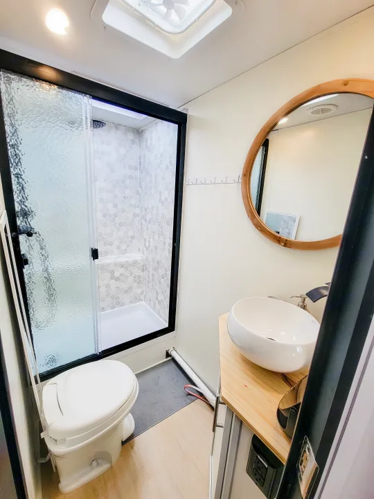Experience comfort in this RV rental bathroom: a tiled shower, compact toilet, and elegant vessel sink vanity.. Forest River Tracer 2022