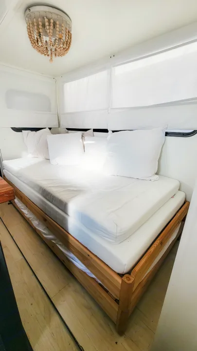 Bright RV rental interior with a bed, white mattresses, wooden frame, and beaded light. White walls and shades visible.. Forest River Tracer 2022