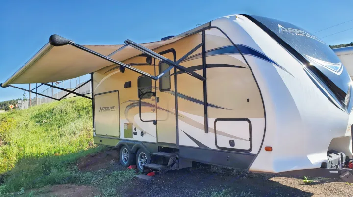 A beige and white Aerolite travel trailer RV rental with an extended awning, parked on gravel.. Dutchmen Aerolite 2017
