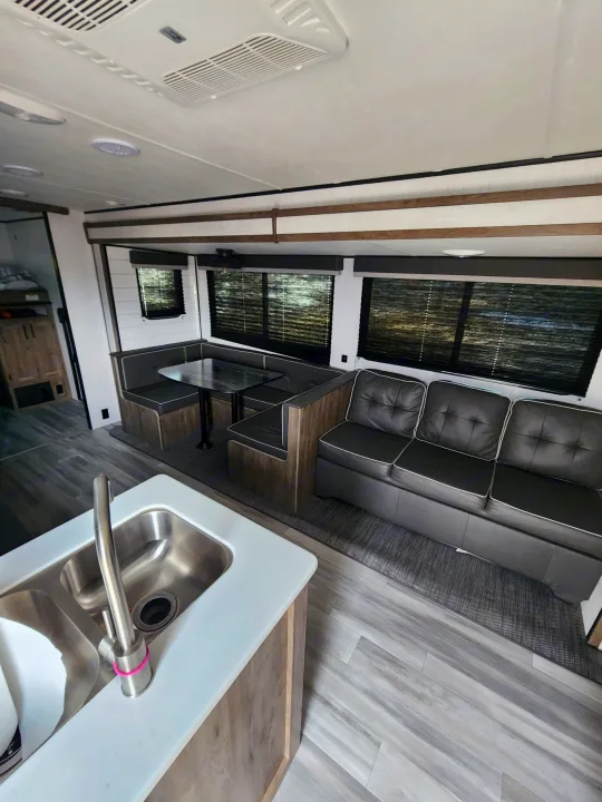 Inside a modern RV rental: dual kitchen sink, comfortable dinette, and sofa. Light wood and dark gray interior.. 5SFPB372XME475890 Pioneer 2021