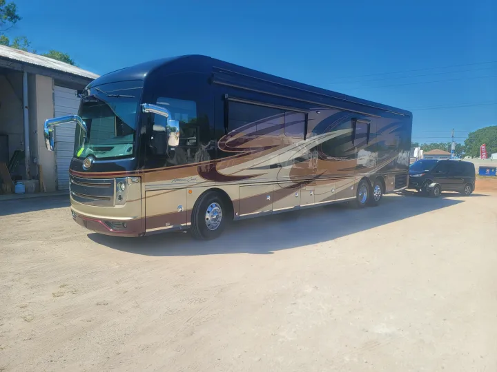 Experience comfort with this luxury RV rental, a spacious motorhome towing a small vehicle on a bright day.. Fleetwood American Eagle 2018