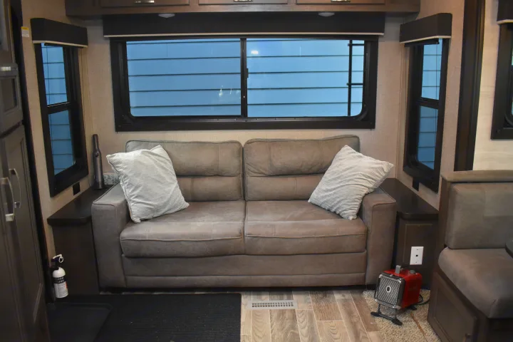 RV rental interior: cozy living space with a grey sofa, windows showing the outside, and a small heater. Ideal for travel.. Jayco Jay Flight SLX Rocky Mountain Edition 2021