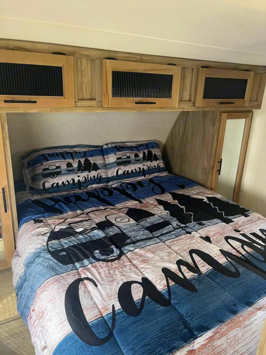 Inside this RV rental's cozy bedroom: Happy Camping bedding, wood cabinets, and a convenient built-in mirror.. Forest River Cherokee Alpha Wolf 2022