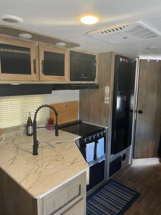 Modern RV rental kitchen features a compact design with sink, stove, microwave, and refrigerator, ideal for travel.. Forest River Cherokee Alpha Wolf 2022