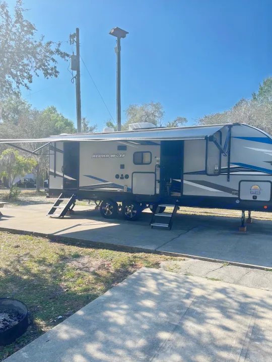 This RV rental is set up at a sunny campsite, with its awning out and steps down, ready for adventure.. Forest River Cherokee Alpha Wolf 2022