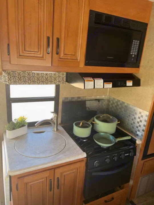 Clean RV rental kitchen with microwave, stove, sink, and new green cookware. Perfect for your next road trip!. Forest River Sunseeker 2016