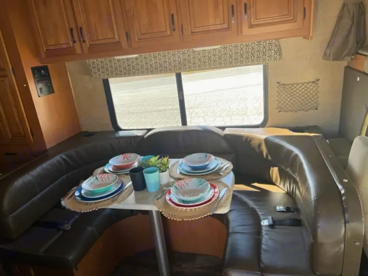 RV rental interior featuring a cozy dinette with U-shaped leather seating and a colorful table setting, ready for meals.. Forest River Sunseeker 2016