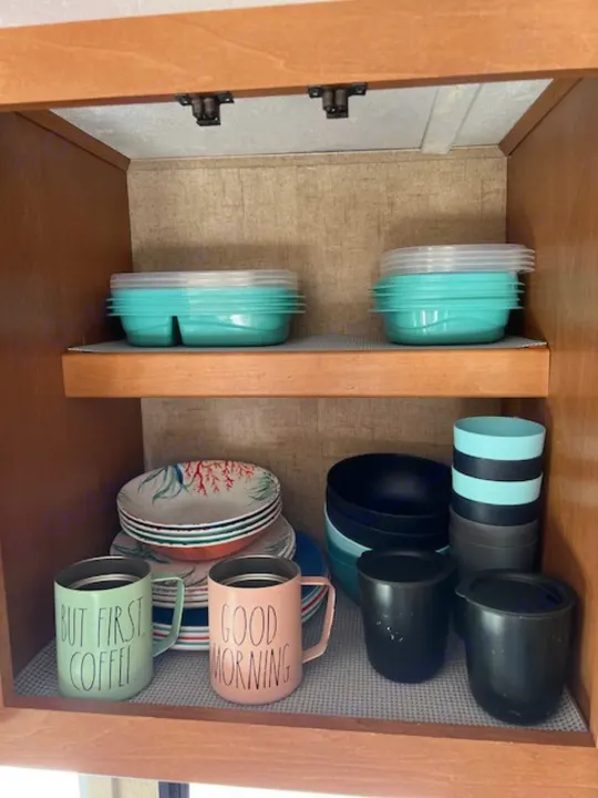 RV rental kitchen cabinet showing organized plates, mugs, bowls, and food storage containers.. Forest River Sunseeker 2016