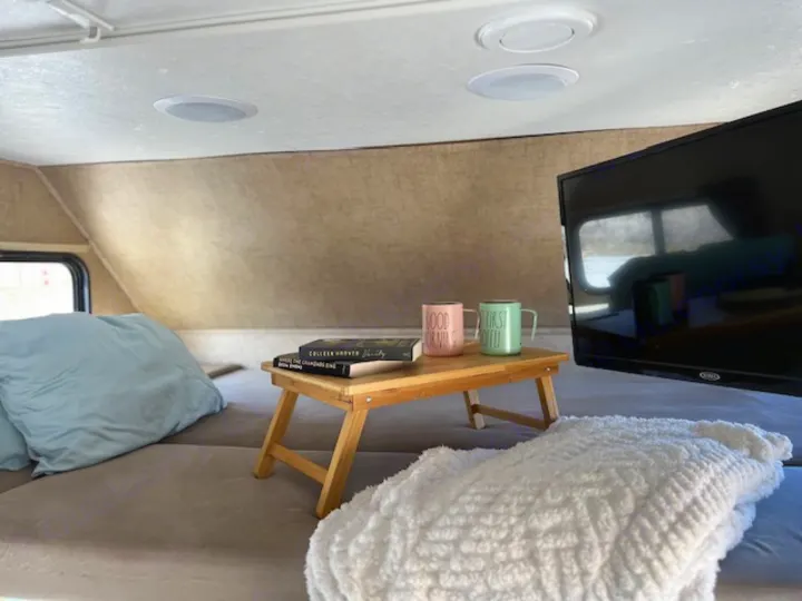 Cozy RV rental interior: bed, TV, and breakfast tray with "GOOD MORNING" coffee mugs and books for a relaxing start.. Forest River Sunseeker 2016