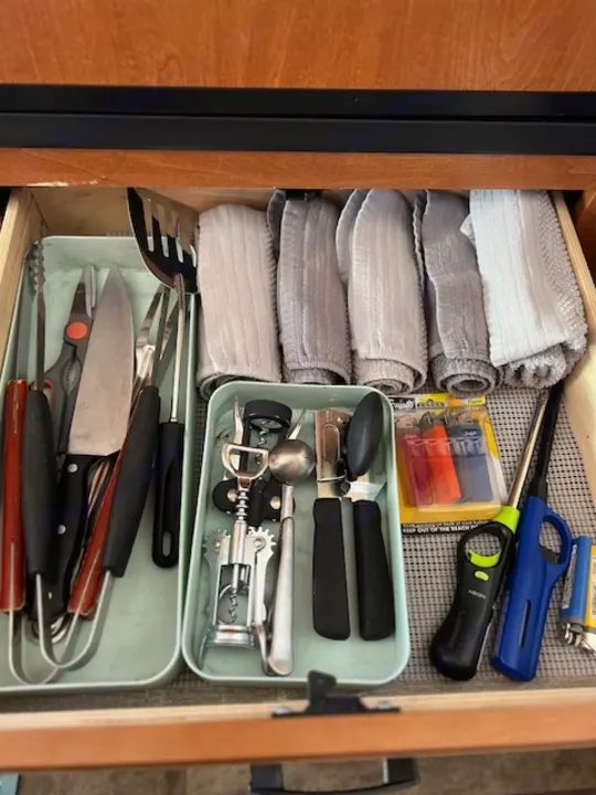 Organized RV rental kitchen drawer with utensils, folded towels, and lighters for camping convenience.. Forest River Sunseeker 2016