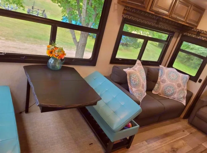 Bright rv rental living space: dining table, teal bench with storage, cozy sofa, and scenic window views.. KZ Durango 2021