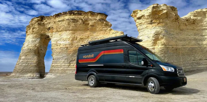 Black Vandoit camper van for RV rental, parked before impressive natural rock formations, including a large arch.. Vandoit DO 2019