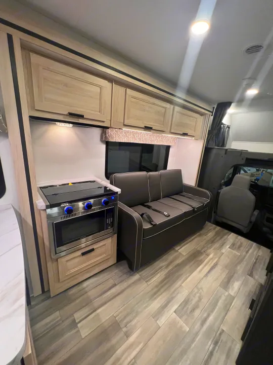 Modern RV rental interior with a compact kitchen, sofa with seatbelts, and light wood-look flooring.. Forest River Sunseeker 2024