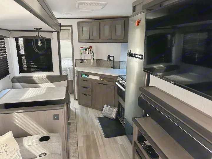 Modern rv rental interior showing a full kitchen with cabinets, sink, and fridge, plus a dining area and a visible bedroom.. Cruiser RV Embrace Ultra Lite 2022