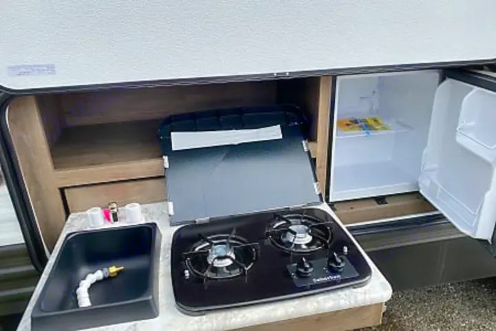 RV rental outdoor kitchen with a sink, two-burner stove, mini-fridge, and storage shelves for convenient outdoor cooking.. Dutchmen Aspen Trail 2020