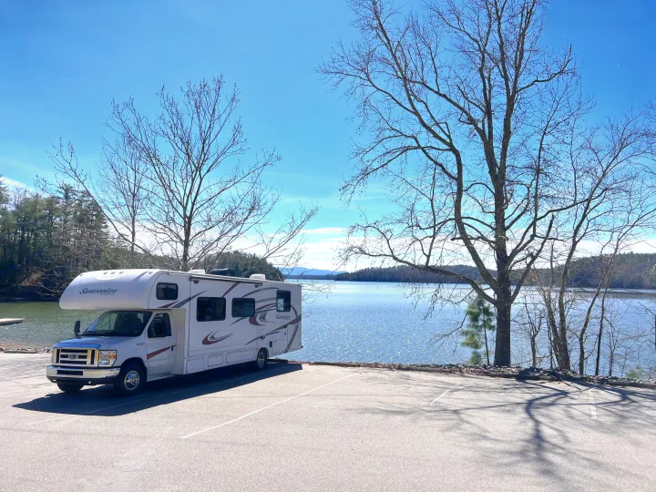 RV rental parked by a sparkling lake on a sunny day, surrounded by bare trees. An ideal setting for outdoor adventures.. Forest River Sunseeker 2016