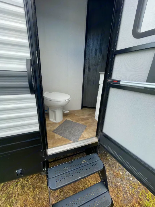 Accessing an RV rental, showing the open doorway, stairs, and interior compact bathroom with a white toilet and light wood floor.. Keystone RV Hideout 2022