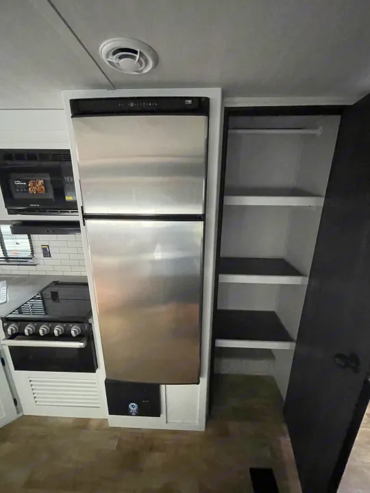 Explore this RV rental's well-equipped kitchen featuring a stainless steel fridge, microwave, stove, and accessible pantry.. Keystone RV Hideout 2022