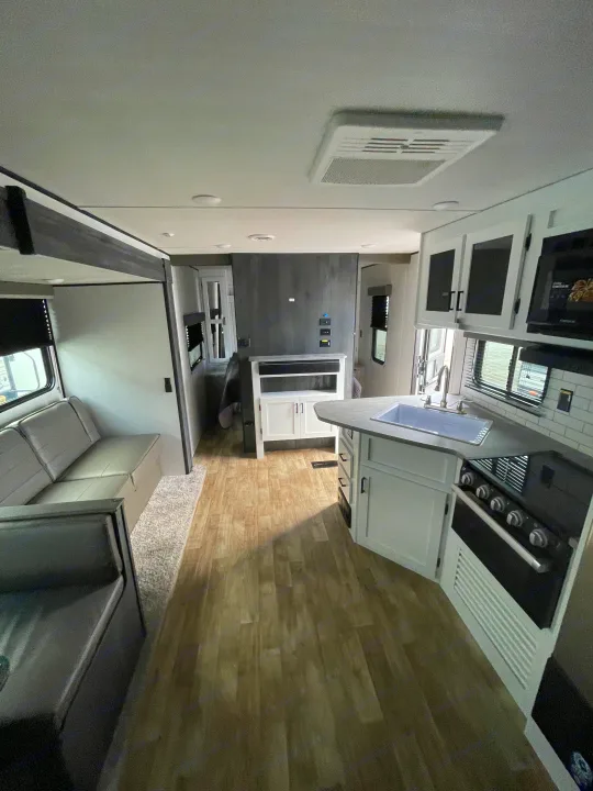 Modern RV rental interior featuring a kitchen island, sink, stove, and a comfortable living area with a sofa.. Keystone RV Hideout 2022