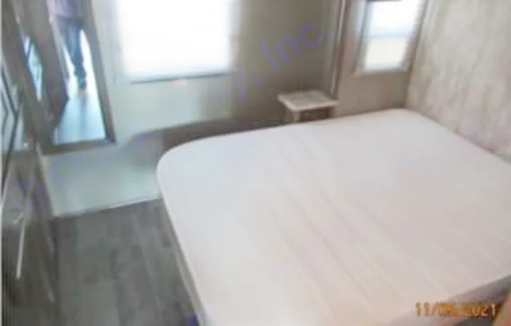 Clear view of an RV rental bedroom. A large bed dominates the right, with dark flooring and a doorway to the left.. Winnebago Intent 2018