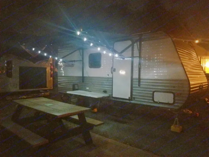 An RV rental unit is brightly lit by string lights at a night campsite, with a picnic table in the foreground.. Coleman Lantern 17B 2023